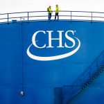 Two people in PPE standing on top of a large blue storage bin with a CHS logo